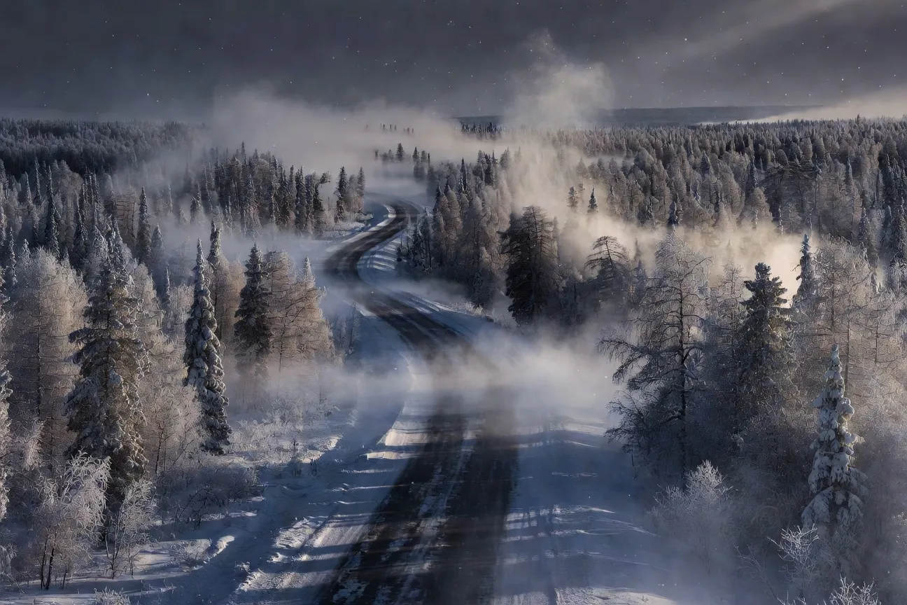 La Route des Os en Yakoutie sous la neige : chaussée glacée traversant une forêt de taïga dense dans un brouillard de froid